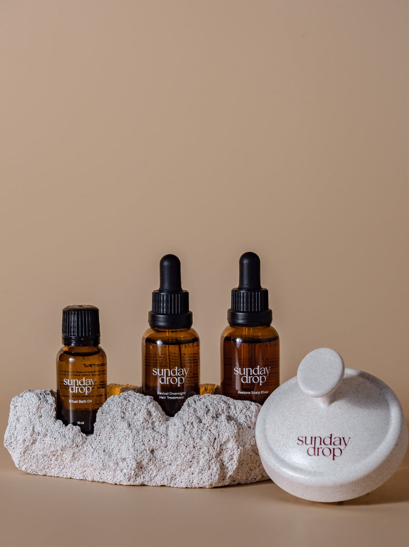 Three 'sunday drop' bottles with droppers on a stone surface against a beige background