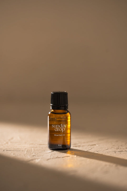 Small amber bottle labeled 'sunday drop' on a textured surface with a neutral background